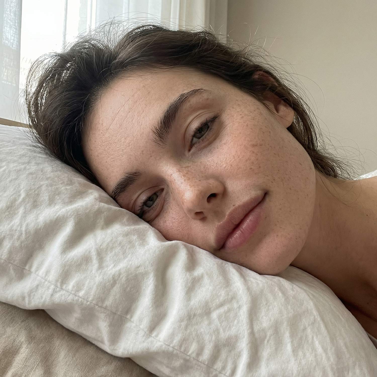 Žena leží na vankúši s unaveným výrazom a jemne otlačenou pokožkou, čo naznačuje nepohodlný alebo nevhodný vankúš počas spánku.